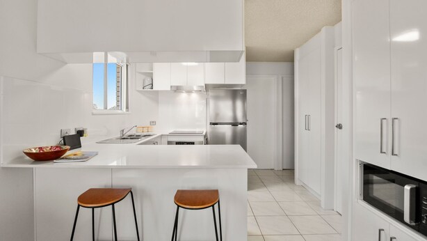 Una cocina moderna con armarios blancos, electrodomésticos de acero inoxidable y una isla central con taburetes.