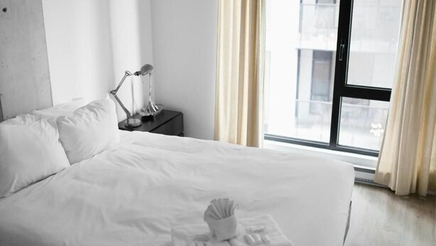 Ein Hotelzimmer mit einem großen Bett, einem Nachttisch mit Lampe und einem Fenster mit Vorhängen.