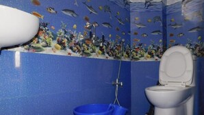 Ein Badezimmer mit blau gefliestem Boden, einer Toilette, einem blauen Eimer und einem Wandgemälde mit Unterwasser-Motiv.