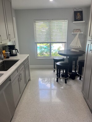 A kitchen with a window, a coffee maker, a small sailboat model, and a bar stool.