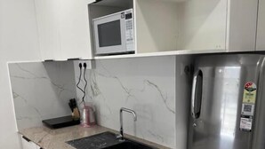 A compact kitchen with a built-in microwave, a stainless steel refrigerator, and a marble countertop sink. - Cornerstone Suites (Aizawl)
