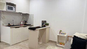 A compact living space with a kitchenette, a small seating area, and a bookshelf. - Cornerstone Suites (Aizawl)