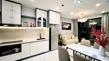 A modern kitchen with white cabinets, a black faucet, and a marble countertop. There is a dining area with a white table and chairs, and a sofa in the background.