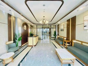 Un hall d’hôtel moderne avec un comptoir d’accueil, des espaces de détente et un lustre.
