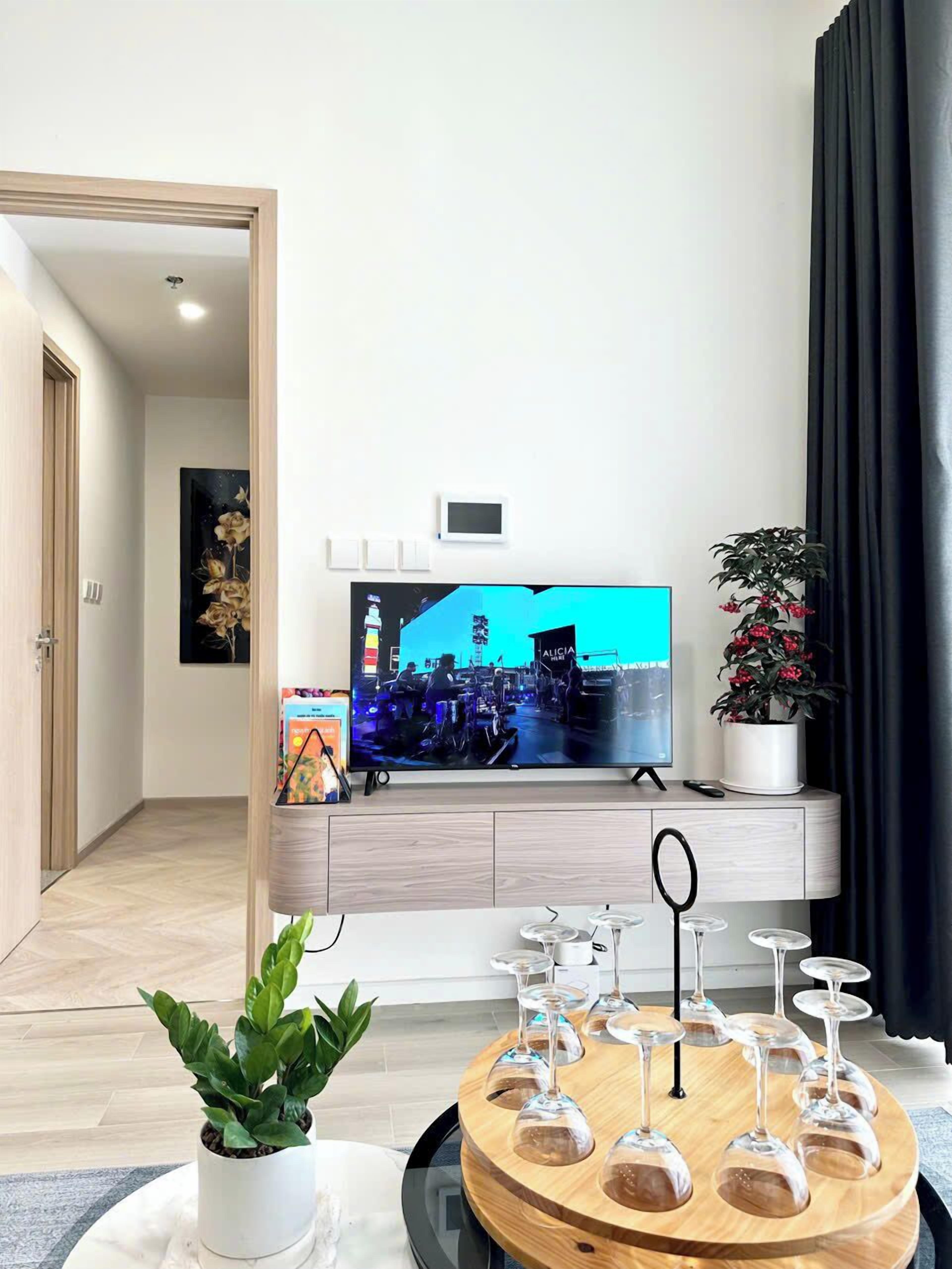 Una sala moderna con televisor de pantalla plana, una planta en maceta y una mesa redonda de madera con copas de vino.
