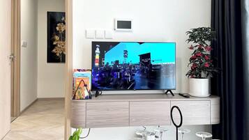 Una sala moderna con televisor de pantalla plana, una planta en maceta y una mesa redonda de madera con copas de vino.