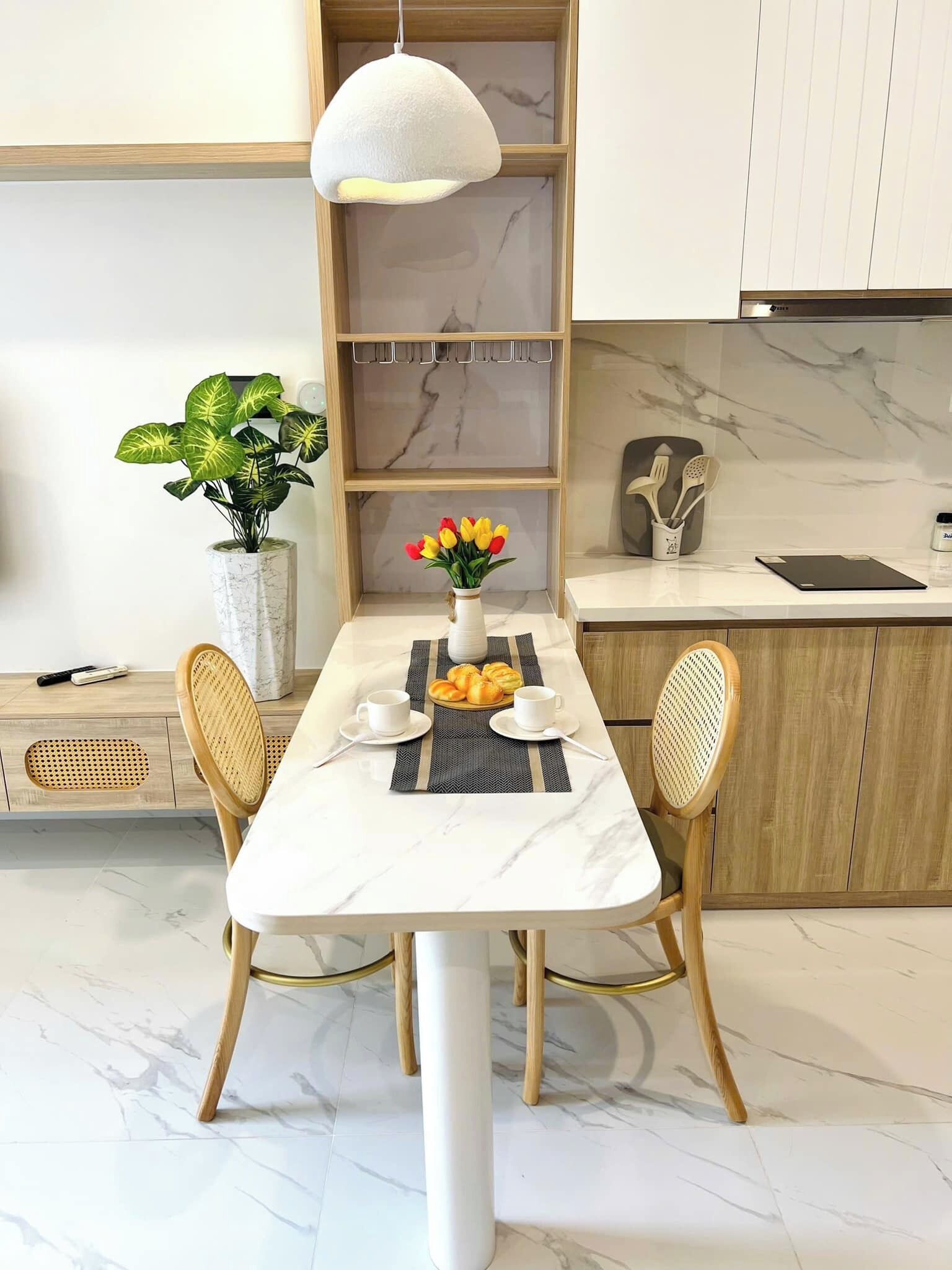 Un comedor con una mesa de mármol, dos sillas, un florero con flores y una lámpara colgante.