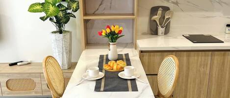Un comedor con una mesa de mármol, dos sillas, un florero con flores y una lámpara colgante.