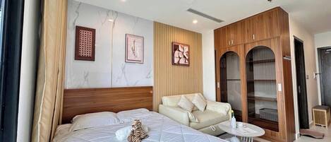 A hotel room with a large bed, a sofa, a small table, and a wardrobe.