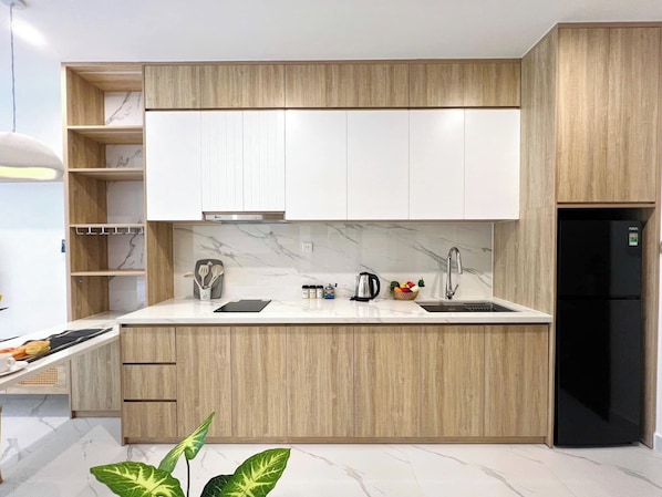 A modern kitchen with wooden cabinets, a marble countertop, a black refrigerator, and a built-in oven. - Saigon Stay at Vinhomes Grand Park (Ho Chi Minh City)