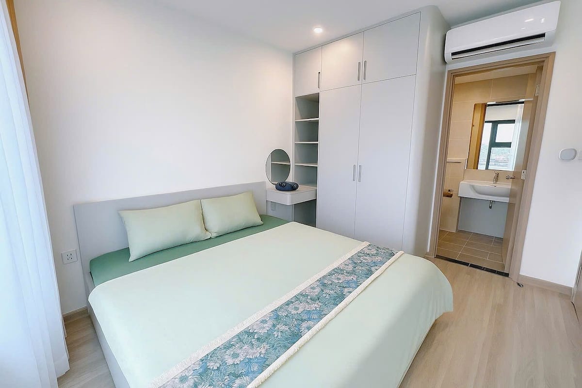 Une chambre à coucher comprenant un lit, une armoire, une table de chevet avec un miroir, et une salle de bain avec un lavabo.