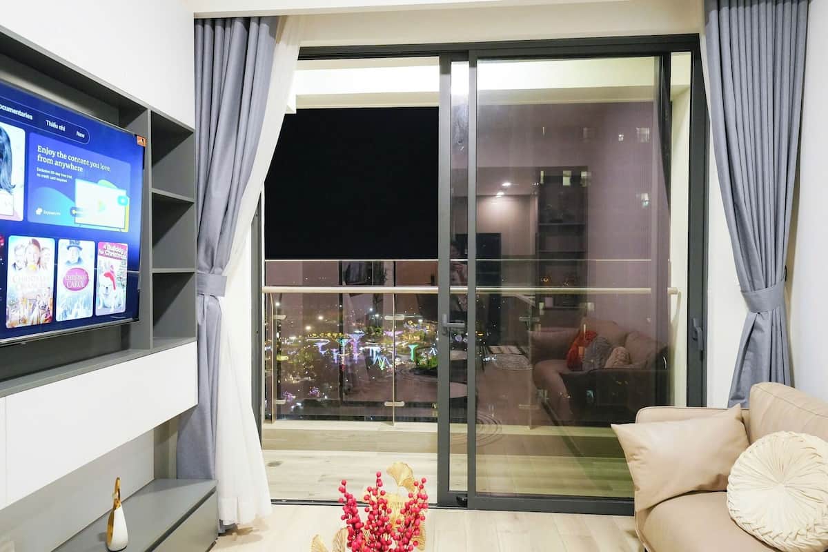 Un salon moderne doté d’un grand téléviseur à écran plat fixé au mur, d’un canapé et d’une porte-fenêtre coulissante donnant sur un balcon avec vue sur la ville.
