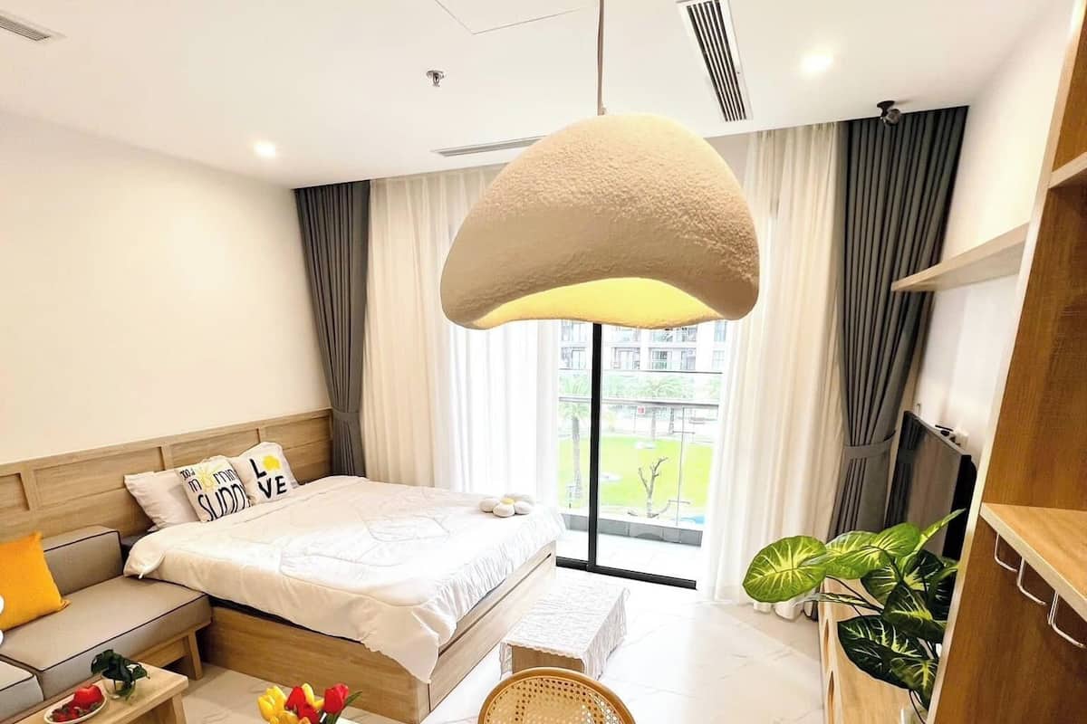 Une chambre d’hôtel moderne dotée d’un grand lit, d’un coin salon avec un canapé et des fauteuils, d’une table à manger agrémentée d’un vase de fleurs et offrant une vue sur l’extérieur.