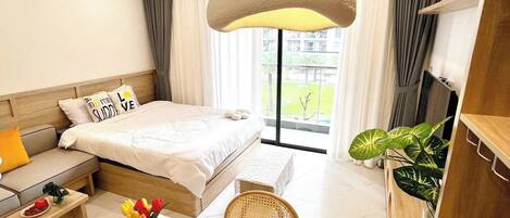 Una habitación de hotel moderna con una cama grande, una zona de estar con sofá y sillones, una mesa de comedor con un jarrón de flores y vistas al exterior.