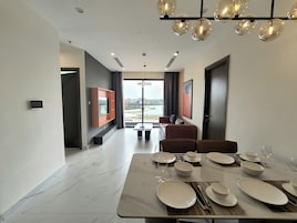 Uma sala de jantar moderna com uma mesa grande posta para quatro pessoas, um sofá e uma televisão fixada na parede.