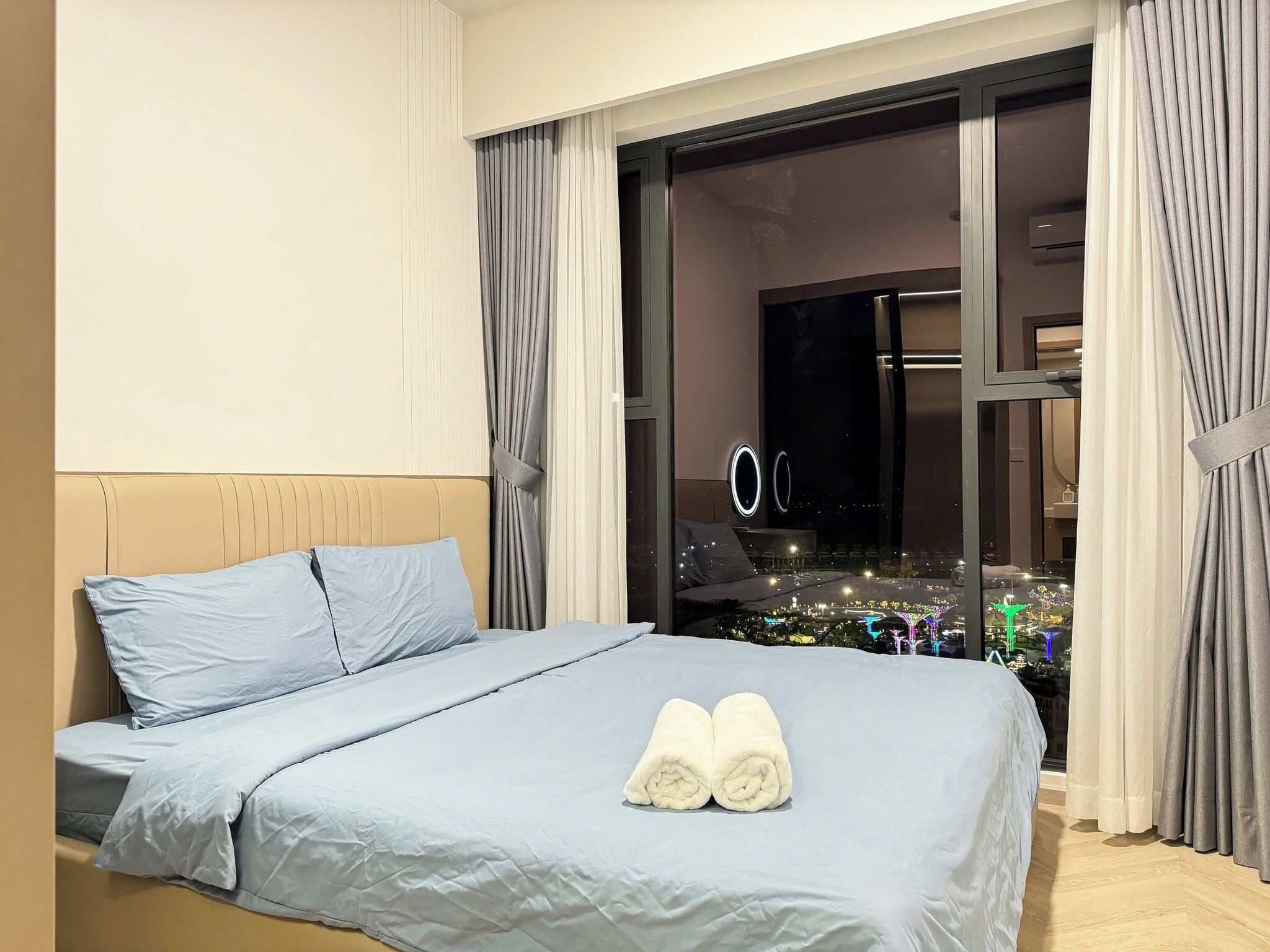A hotel room with a bed, a view of a cityscape through a large window, and a TV on the opposite wall.