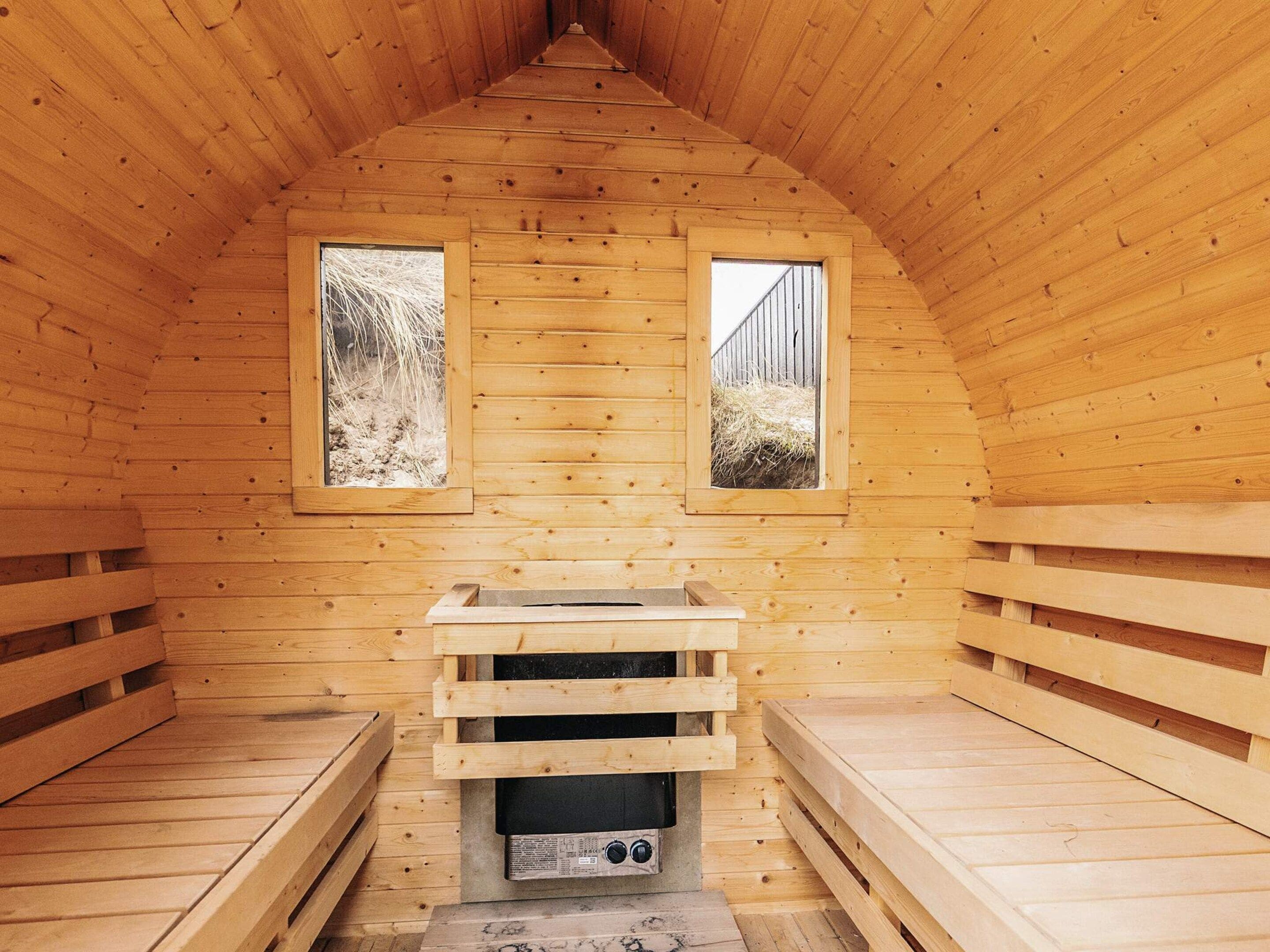 A wooden sauna with two windows, a bench, and a sauna heater.