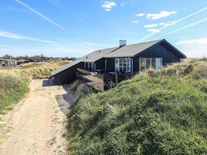 A modern building with a sloped roof, large windows, and a covered outdoor seating area. - 5 Star Holiday Home in Lokken (Lokken)