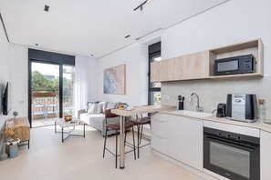 A modern kitchen with a built-in microwave, oven, and coffee maker. There is a dining area with a table and chairs, and a sofa in the living room.