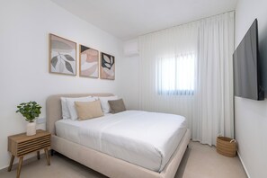 A bedroom with a bed, a TV, a plant, and artwork on the wall.