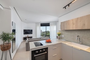 A modern kitchen with a built-in oven, a dining area with a sofa, and a large window with curtains.