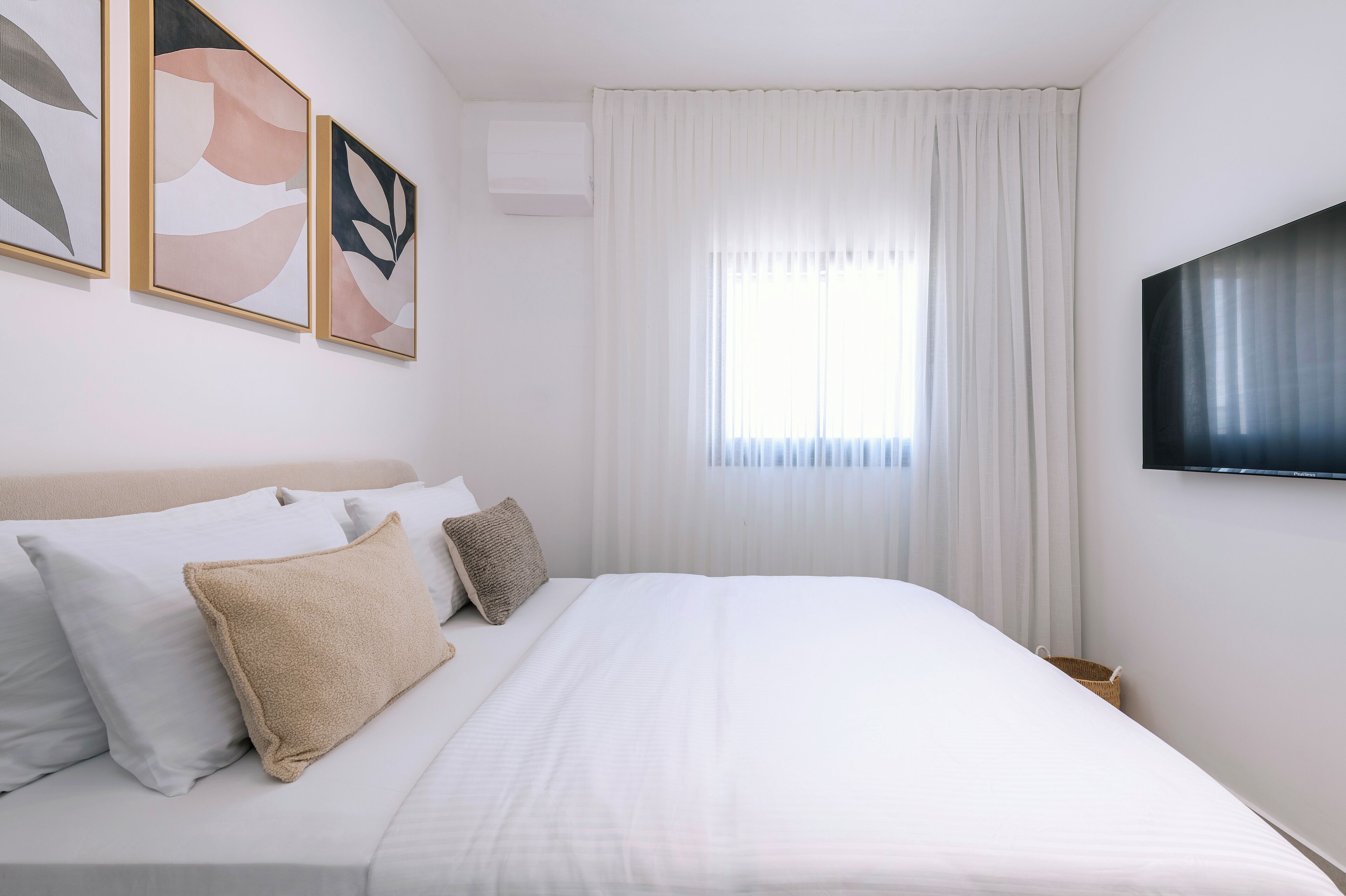 A hotel room with a bed, pillows, a TV, and artwork on the wall.