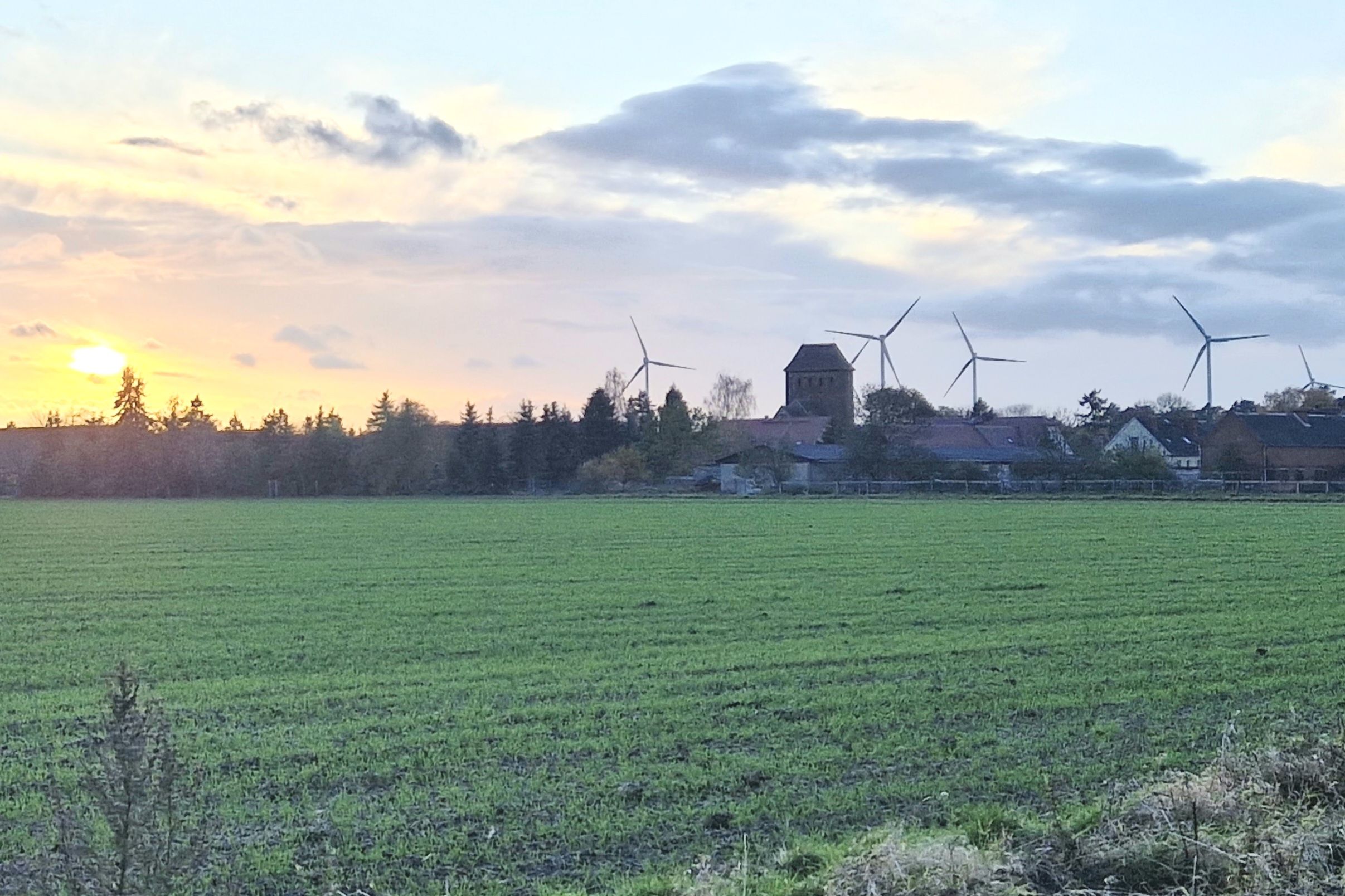 Paesaggio rurale con turbine eoliche, un campo e un edificio con una torre.