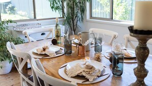 A dining table set with plates, glasses, and a candle, surrounded by chairs and a large window with a view of greenery. - Luxurious & spacious retreat near Swan Lake (Sussex Inlet)