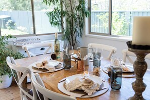 Een eettafel gedekt met borden, glazen en een kaars, omringd door stoelen en een groot raam met uitzicht op groen.