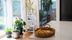 A kitchen with a white countertop, a wicker basket with fruits, and a white shelving unit with plants and books. - Luxurious & spacious retreat near Swan Lake (Sussex Inlet)