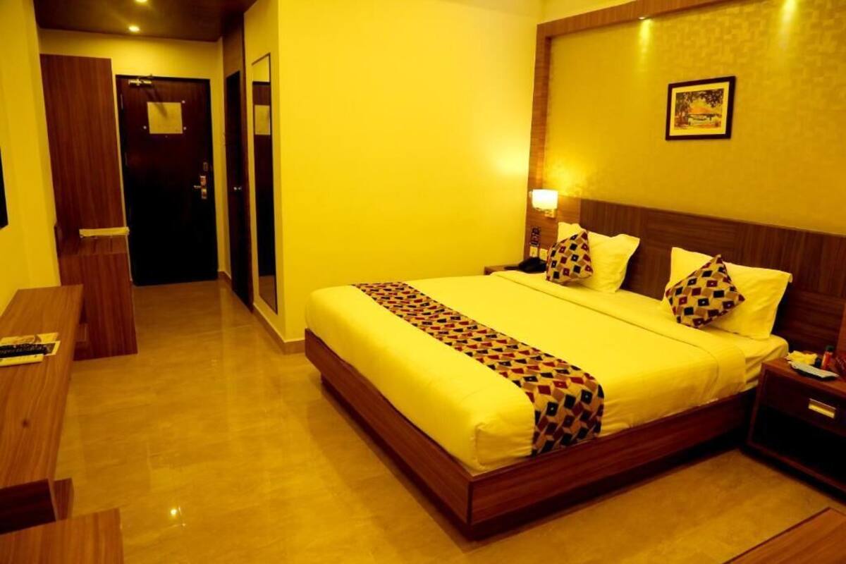 Una habitación de hotel con una cama grande, mesitas de noche, un banco de madera y una puerta.
