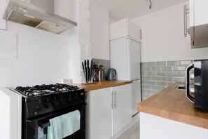 A modern kitchen with a gas stove, white cabinets, a stainless steel range hood, and a tiled backsplash. - Snug 1BDR City Retreat in West London (Greater London)