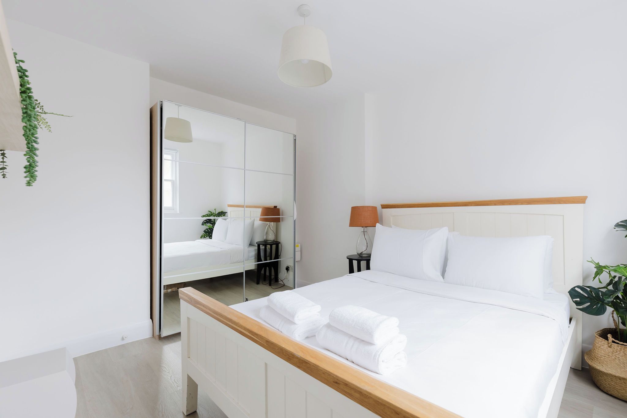 A modern bedroom with a bed, bedside tables, a mirror, and a hanging light fixture.