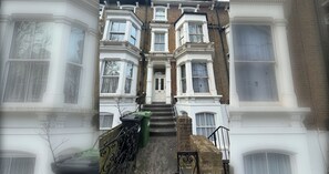 A row of townhouses with a central entrance, a green bin, and a brick wall. - Snug 1BDR City Retreat in West London (Greater London)