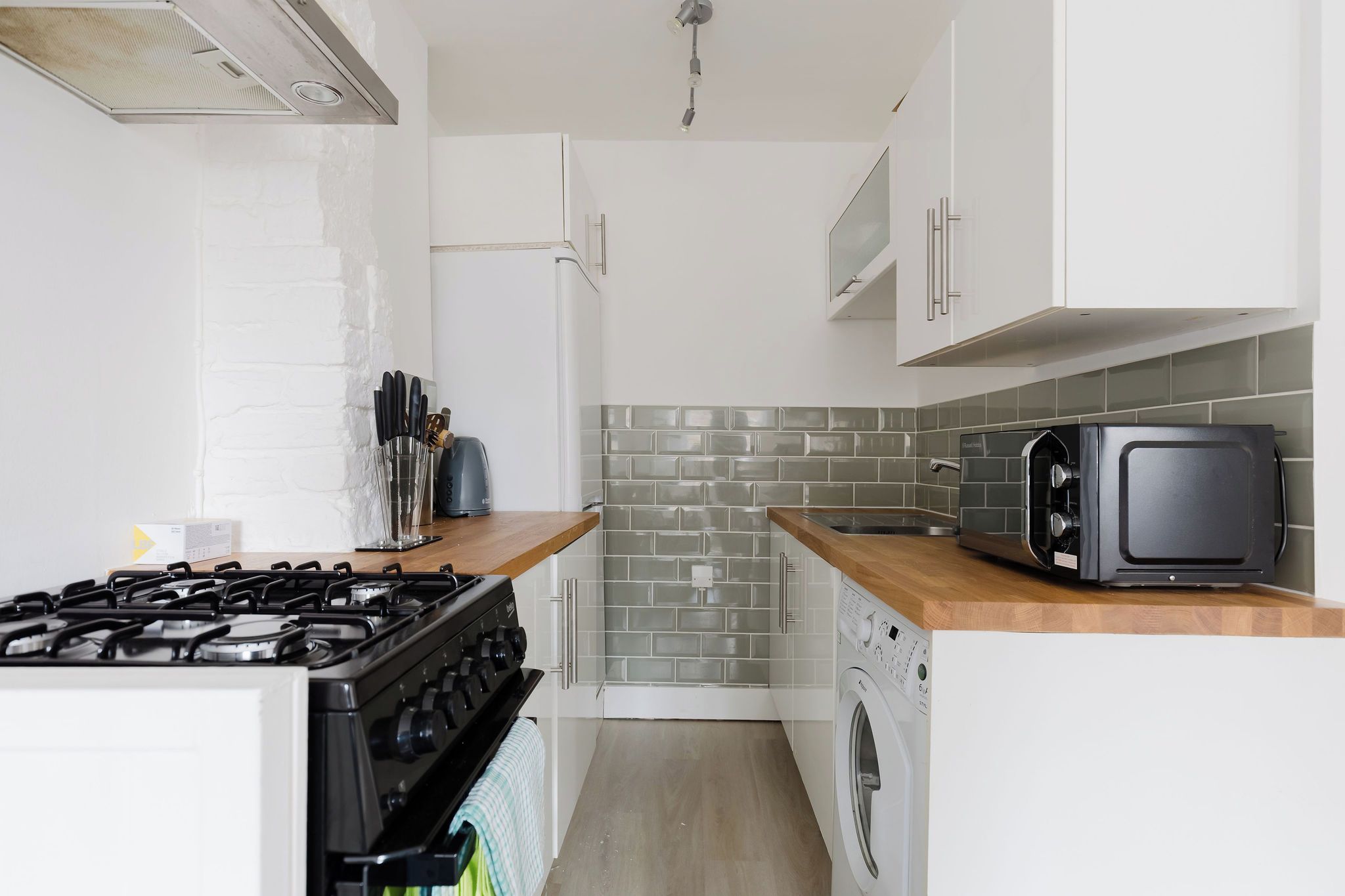 A compact kitchen with a gas stove, a microwave, a toaster, and a washing machine.