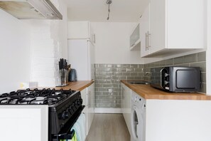 A compact kitchen with a gas stove, a microwave, a toaster, and a washing machine. - Snug 1BDR City Retreat in West London (Greater London)