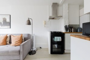 En moderne stue med en grå sofa, en gulvlampe og et køkken med komfur, ovn og mikroovn.