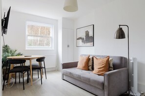 En moderne stue med en grå sofa, et spisebord med stole, en pendel og en radiator.