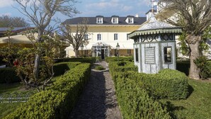 Un edificio con un vialetto lastricato, un gazebo e siepi curate.