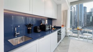Une cuisine moderne avec un plan de travail bleu, un évier en acier inoxydable et une vue sur de hauts immeubles à travers de grandes fenêtres.