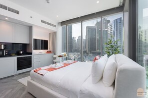 A modern bedroom with a large bed, a kitchen area, and a city view. - Réveille Face au Burj Khalifa Vu Canal & Piscine (Dubai)
