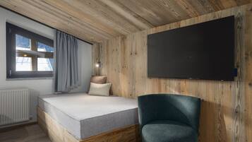 Un dormitorio con techo de madera, una cama con colchón y almohadas, una silla, una ventana con cortinas y un televisor de pantalla plana montado en la pared.