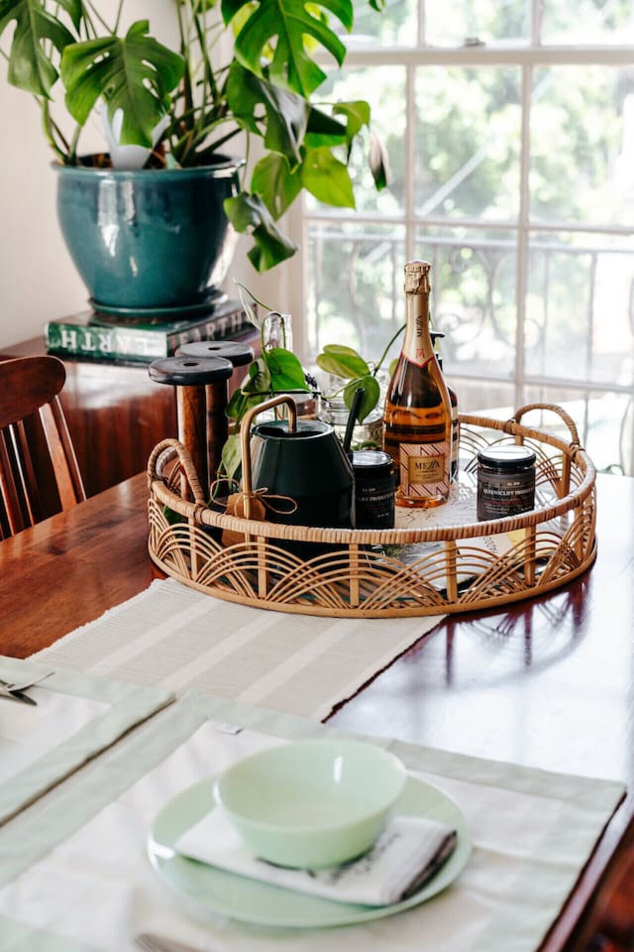 A dining table with a wicker tray holding a bottle, a jar, and a teapot.
