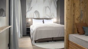 A bedroom with a bed, a wooden headboard, a nightstand, and a small seating area with cushions. - Familienapartment mit 2 SZ fur 8 Personen (Kaprun)