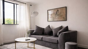 Una sala de estar moderna con un sofá gris, una mesa de centro redonda, una lámpara de pie y un cuadro en la pared.