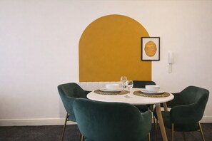 Zona pranzo con un tavolo rotondo, quattro sedie verdi, ciotole bianche e un bicchiere di vino.