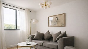 Una sala de estar moderna con un sofá gris, una mesa de centro redonda, una lámpara de pie y una obra de arte enmarcada en la pared.