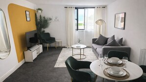 Una sala de estar moderna con un sofá, sillas, una mesa de comedor, una mesa de centro y un amplio ventanal con cortinas.