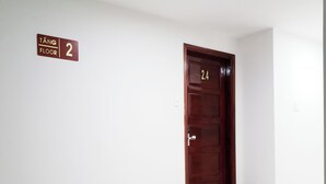 Un couloir avec une pancarte indiquant le deuxième étage, une porte en bois portant le numéro 24 et un sol recouvert de carreaux blancs.