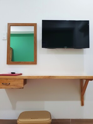 Uma escrivaninha de madeira com uma televisão montada acima, um espelho, uma gaveta e um banquinho.